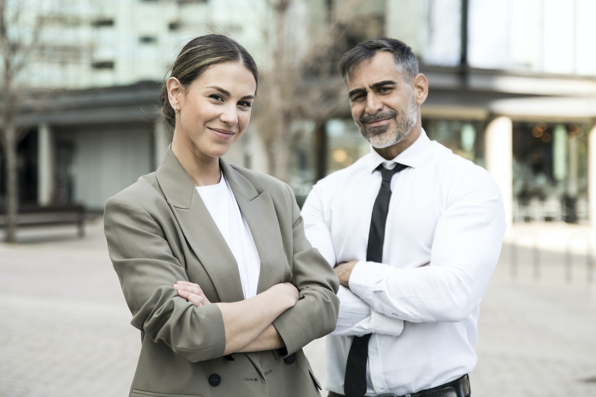 Confident and smiling business people looking at camera in the street with their arms crossed. Young