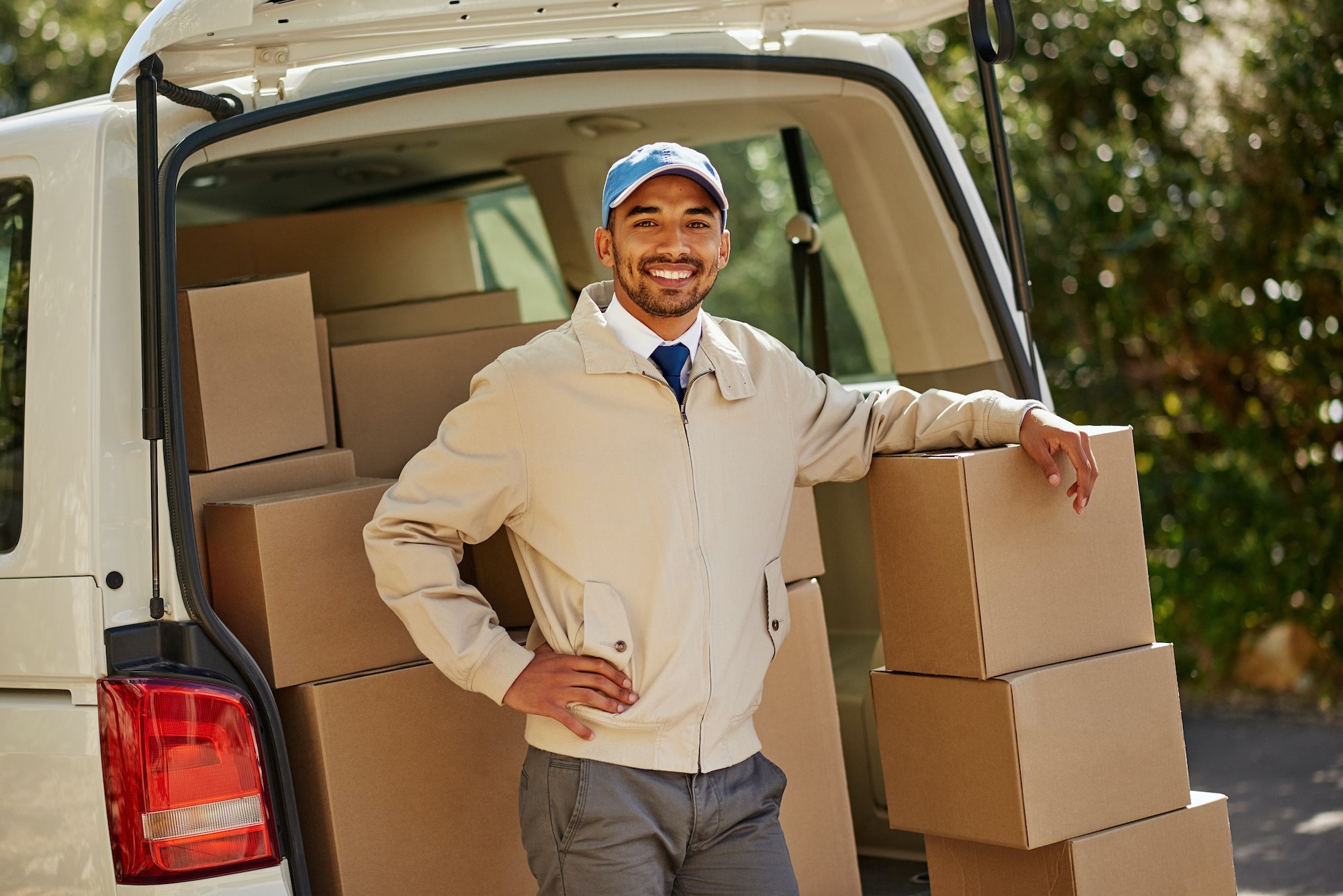 Portrait of a friendly delivery man unloading cardboard boxes from his van